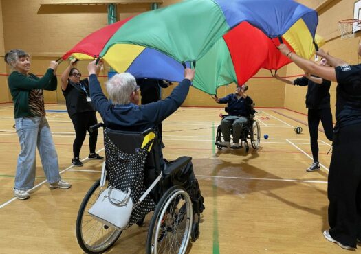 Person in a wheelchair taking part in a parachut game in a sports hall